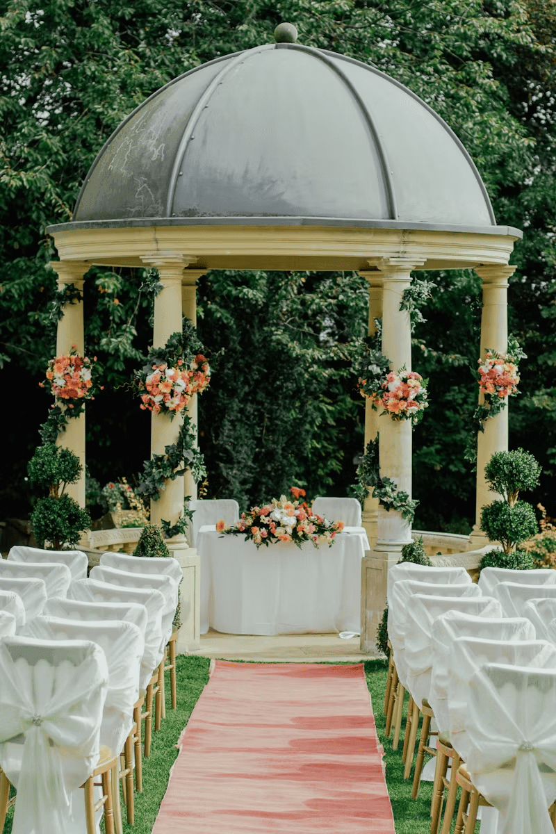Outdoor wedding ceremony aisle with pink runner and floral-decorated gazebo